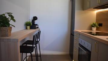 Una cocina compacta con encimera de madera, dos sillas negras, horno empotrado y una pequeña planta en maceta.