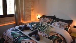A bed with a tropical leaf pattern bedspread, a headboard, and two bedside lamps. - Apartment & Boutique Meraki 1 bedroom. (Ontinyent)