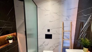 A modern bathroom with a glass shower enclosure, a white toilet, a wooden vanity with a bathtub, and a marble backsplash. - Apartment & Boutique Meraki 1 bedroom. (Ontinyent)