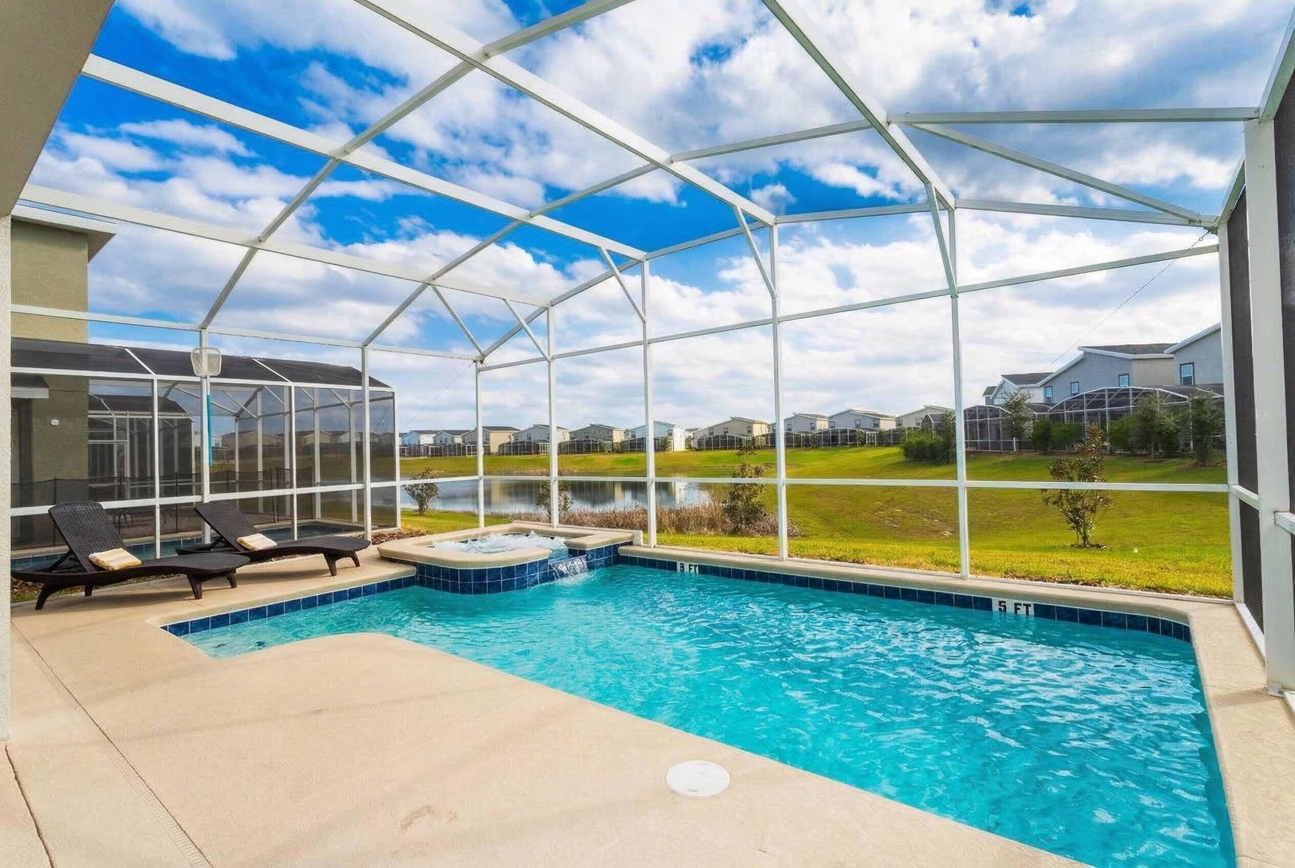 A covered outdoor swimming pool with lounge chairs, a hot tub, and a view of residential buildings.