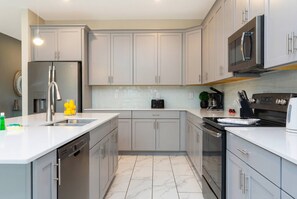 A modern kitchen with grey cabinets, stainless steel appliances, and a white countertop. - Luxury 6BR Resort Villa Near Disney (Kissimmee)
