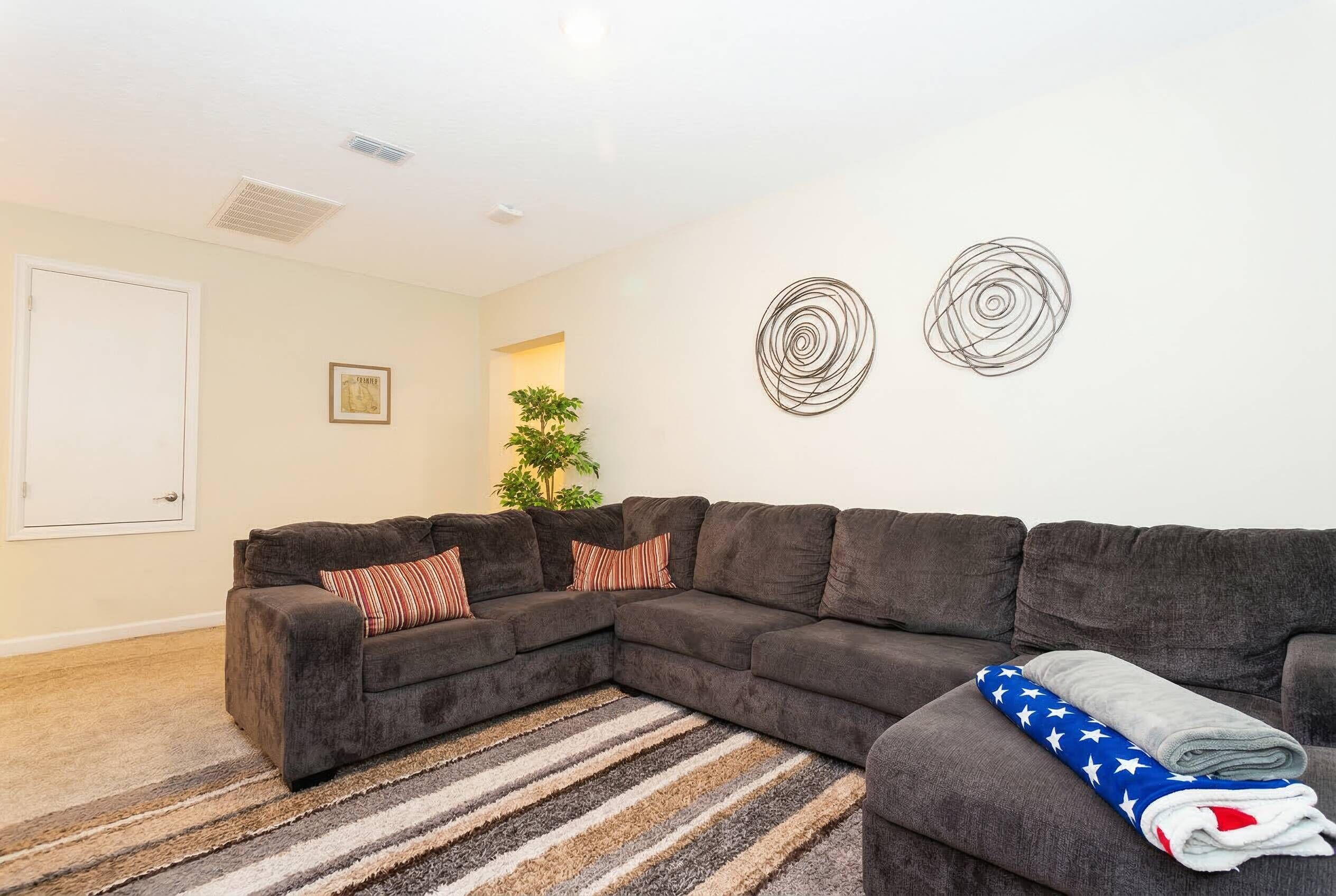 A living room with a sectional sofa, a striped rug, and two wall art pieces.