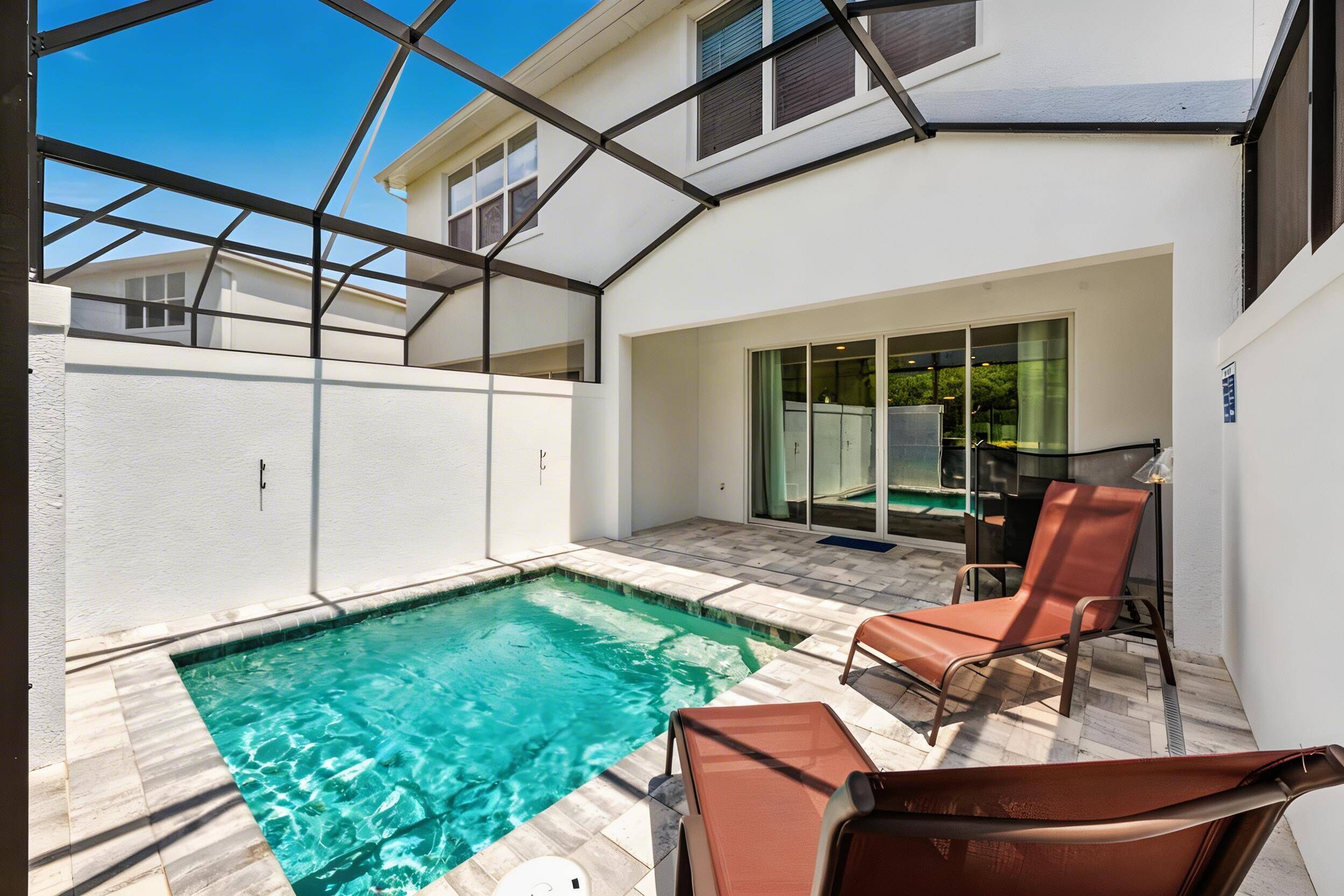 A swimming pool with a glass enclosure, a lounge chair, and a patio area with a table.