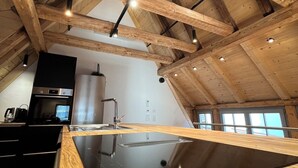 A modern kitchen with wooden beams, a black countertop, and stainless steel appliances. - Altstadt Maisonette Karlstadt - Modern charm in the heart of the old town (Karlstadt)