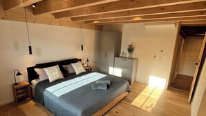 A bedroom with a wooden ceiling, a bed with a blue bedspread, a nightstand with a lamp, and a wardrobe. - Altstadt Maisonette Karlstadt - Modern charm in the heart of the old town (Karlstadt)