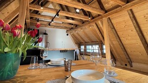 A dining area with a wooden table set for two, a vase of red tulips, and a view of the kitchen in the background. - Altstadt Maisonette Karlstadt - Modern charm in the heart of the old town (Karlstadt)