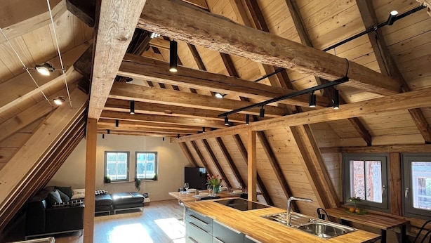 A spacious attic with a wooden ceiling, a central kitchen island, and a seating area with a sofa and a dining table. - Altstadt Maisonette Karlstadt - Modern charm in the heart of the old town (Karlstadt)