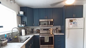 Une cuisine de taille réduite avec des meubles de couleur bleu foncé, des appareils en acier inoxydable et un plancher en bois.