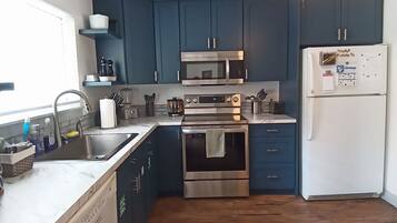 A compact kitchen with dark blue cabinets, stainless steel appliances, and a wooden floor.