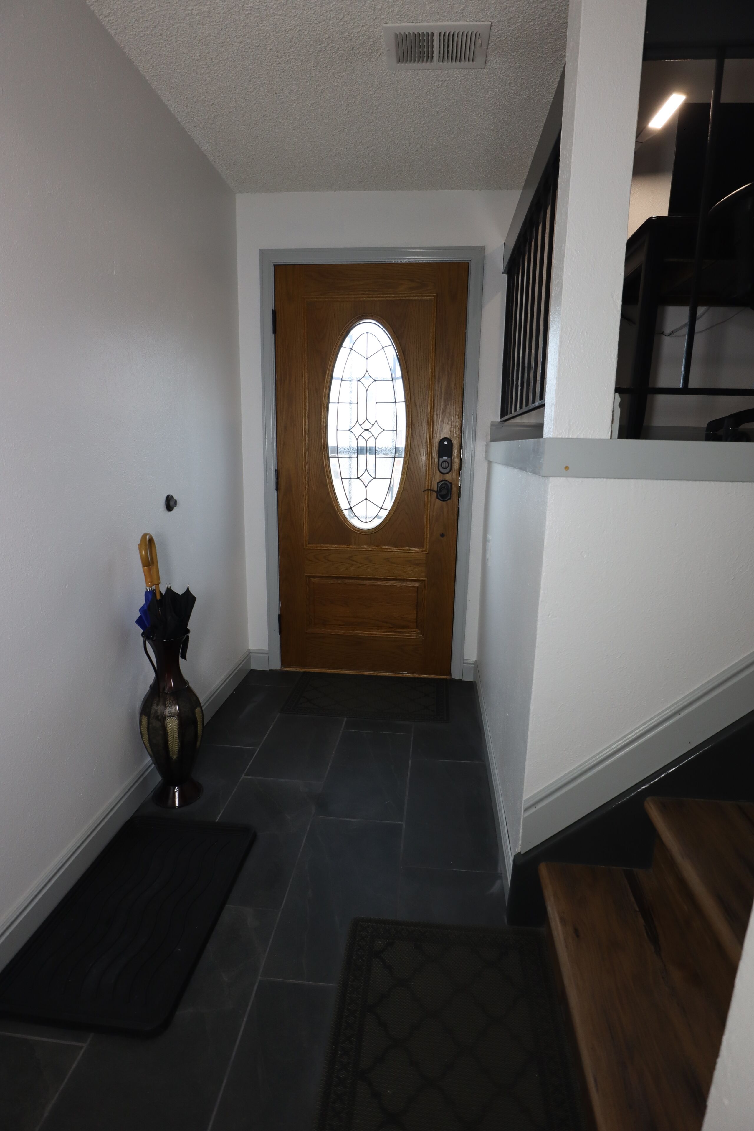 A hallway with a wooden door, a vase with flowers, and a doormat.