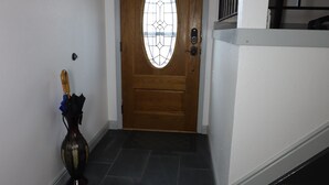 Un couloir avec une porte en bois, un vase rempli de fleurs et un paillasson.