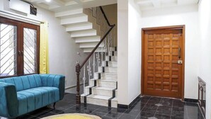 A staircase with a wooden handrail, a blue sofa, a wooden door, and a yellow rug. - THE PUNE STORY HOSTEL (Pune)