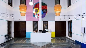 A reception area with a white counter, two hanging lamps, and a colorful mural on the wall. - THE PUNE STORY HOSTEL (Pune)