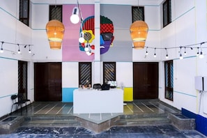 A reception area with a white counter, two hanging lamps, and a colorful mural on the wall. - THE PUNE STORY HOSTEL (Pune)
