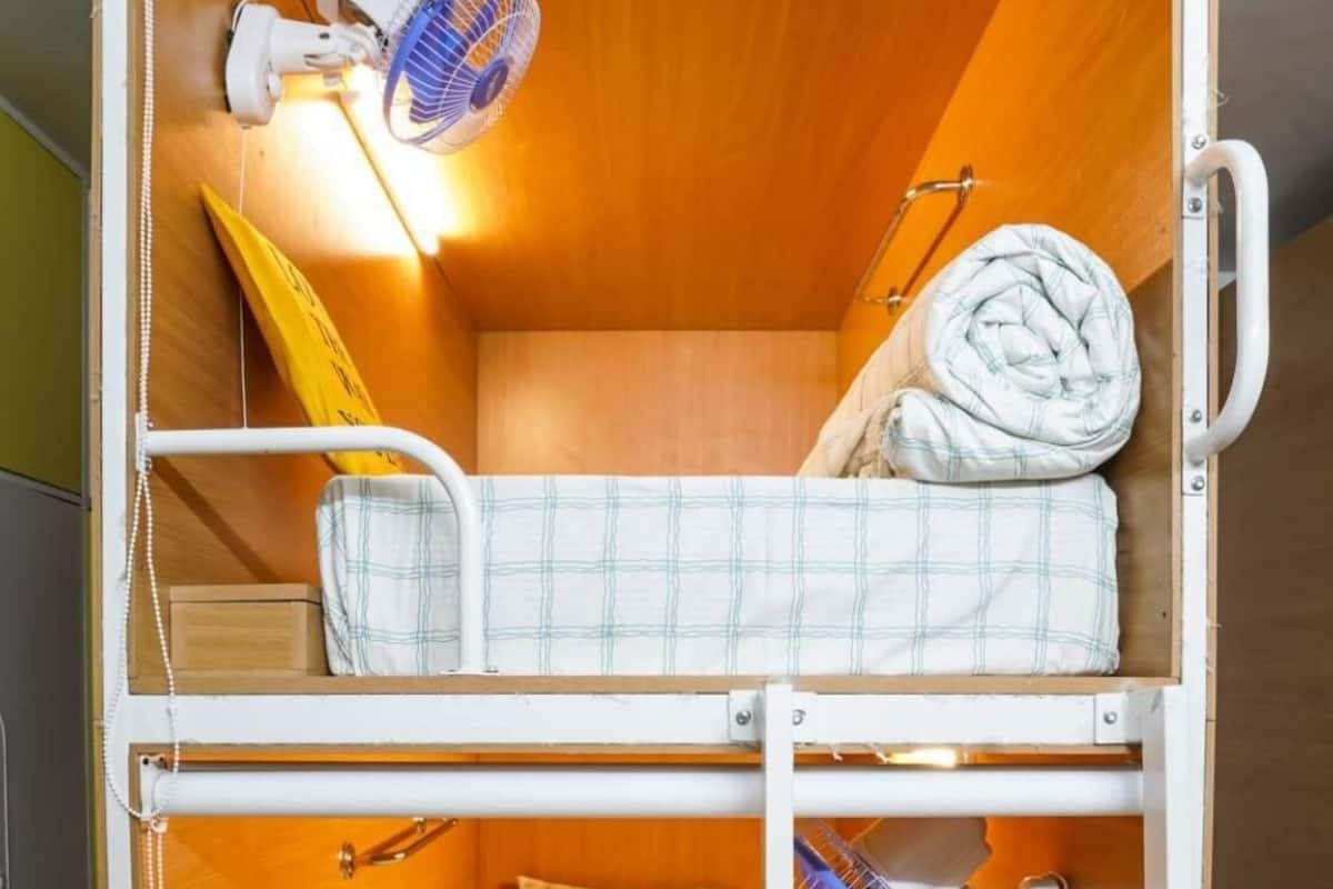Une chambre avec un lit superposé, un ventilateur de plafond, une petite table et une étagère avec une serviette.