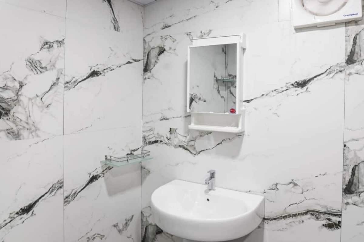 Une salle de bain avec un lavabo sur colonne blanc, un miroir et un luminaire au plafond.