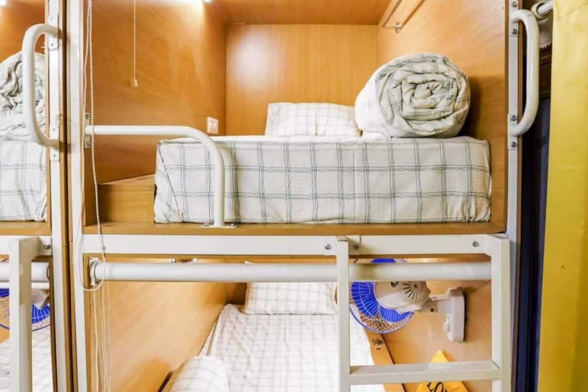 Une chambre avec un lit superposé, un ventilateur, une serviette jaune et un luminaire fixé au mur.