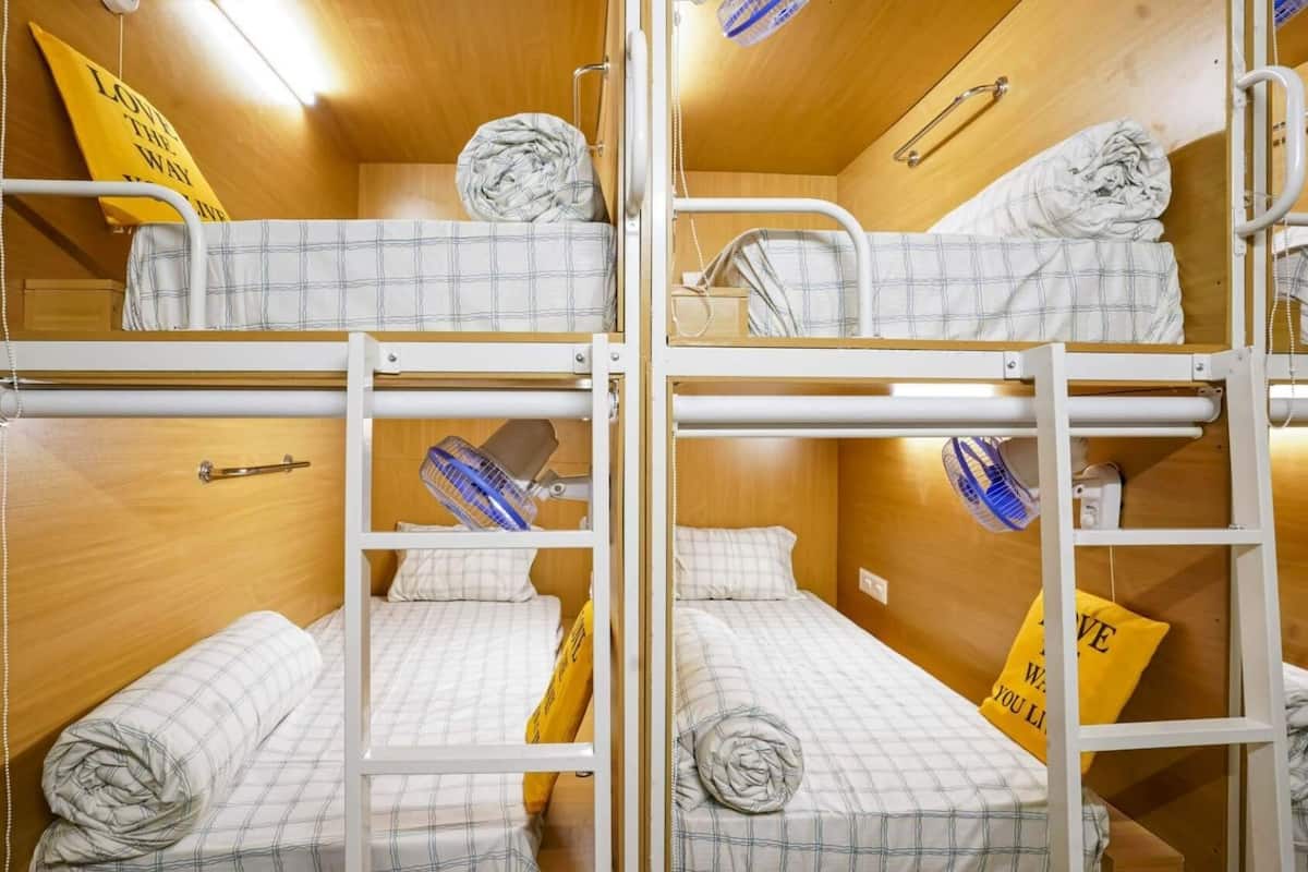 Une chambre avec un lit superposé, un mur en bois, un ventilateur et un oreiller jaune orné d’un motif.