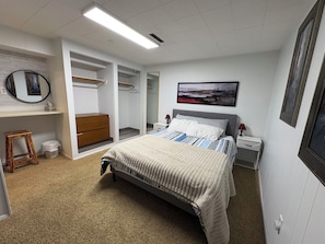 A bedroom with a bed, bedside tables, a wardrobe, a small stool, and a framed picture on the wall.