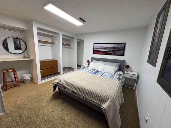 A bedroom with a bed, bedside tables, a wardrobe, a small stool, and a framed picture on the wall.