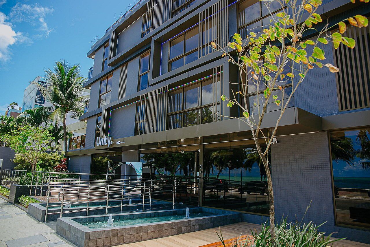 A modern building with a large glass facade, a rooftop pool, and a landscaped area with palm trees.