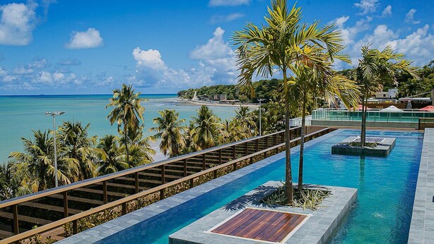 A swimming pool with a wooden deck, palm trees, and a view of the beach. - Unity #110 - Apartment by the sea by Carpediem (João Pessoa)