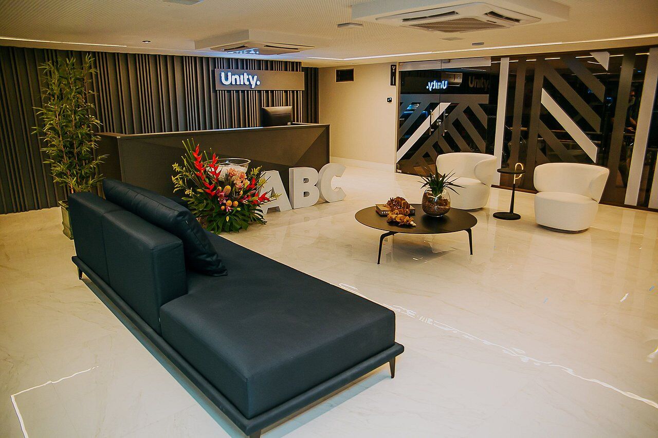 A modern reception area with a black sofa, white chairs, a reception desk, and a large 'Unity' sign.