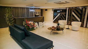 A modern reception area with a black sofa, white chairs, a reception desk, and a large 'Unity' sign. - Unity #110 - Apartment by the sea by Carpediem (João Pessoa)