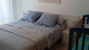 Een slaapkamer met een bed, kussens, een deken, een ledikant, een wanddecoratie en een raam met gordijnen.