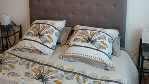 Een slaapkamer met een gebobbelde hoofdbord, beddengoed met bloemenprint, een macramé wandhanger en een ingelijst kunstwerk.