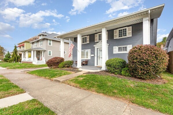 A two-story residential house with a front porch, a flag, and well-maintained landscaping.