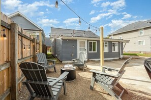 A backyard with Adirondack chairs, a fire pit, and string lights.