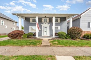 A two-story house with a front porch, a flag, and a well-maintained lawn.