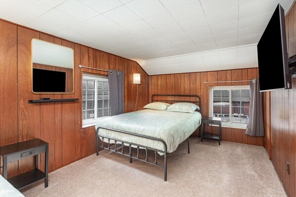 A bedroom with a bed, a bedside table, a wall-mounted TV, and a window with curtains.