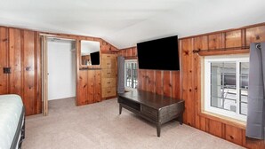 Une chambre avec des lambris en bois, un lit, une télévision, une commode et une fenêtre.