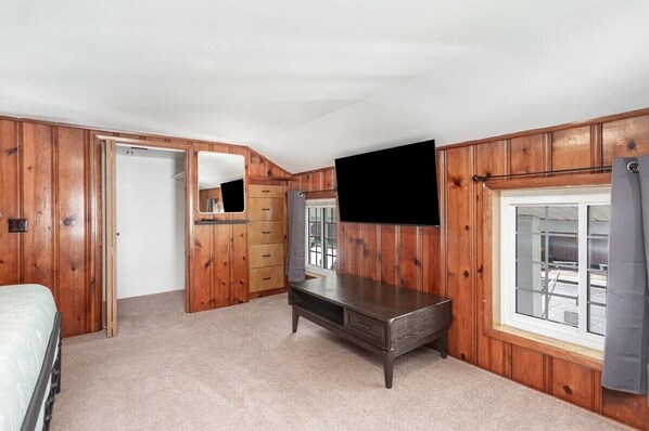 A bedroom with wooden paneling, a bed, a TV, a dresser, and a window.