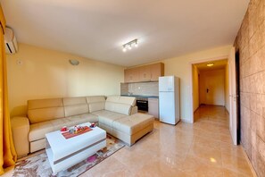 A modern living room with a beige sectional sofa, a white coffee table, and a kitchen area with a refrigerator and oven.