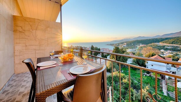 A balcony with a table set for two, overlooking a scenic view of a coastal landscape during sunset. - Apartman ZIS 5D (Opština Bar)