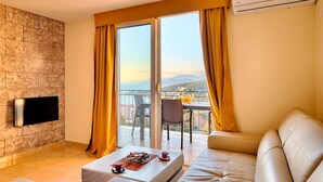 A modern living room with a stone wall, a flat-screen TV, a sofa, a coffee table, and a balcony with a table and chairs. - Apartman ZIS 5D (Opština Bar)