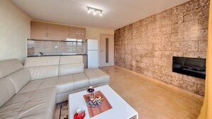 A modern living room with a beige sofa, a coffee table with snacks, and a kitchen in the background. - Apartman ZIS 5D (Opština Bar)