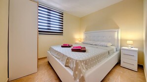 A bedroom with a bed, bedside tables, a wardrobe, and a window with blinds. - Apartman ZIS 5D (Opština Bar)