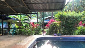 A covered outdoor area with a swimming pool, surrounded by lush greenery and a small seating area. - Ojochal, Costa Rica
artist owned property, extensive gardens and pool (Ojochal)