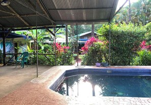 Ein überdachter Außenbereich mit Swimmingpool, umgeben von üppiger Vegetation und einer kleinen Sitzecke.