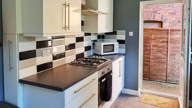 A modern kitchen with white cabinets, a black and white checkered backsplash, a built-in microwave, and a gas stove. - Perry Road (Nottingham)