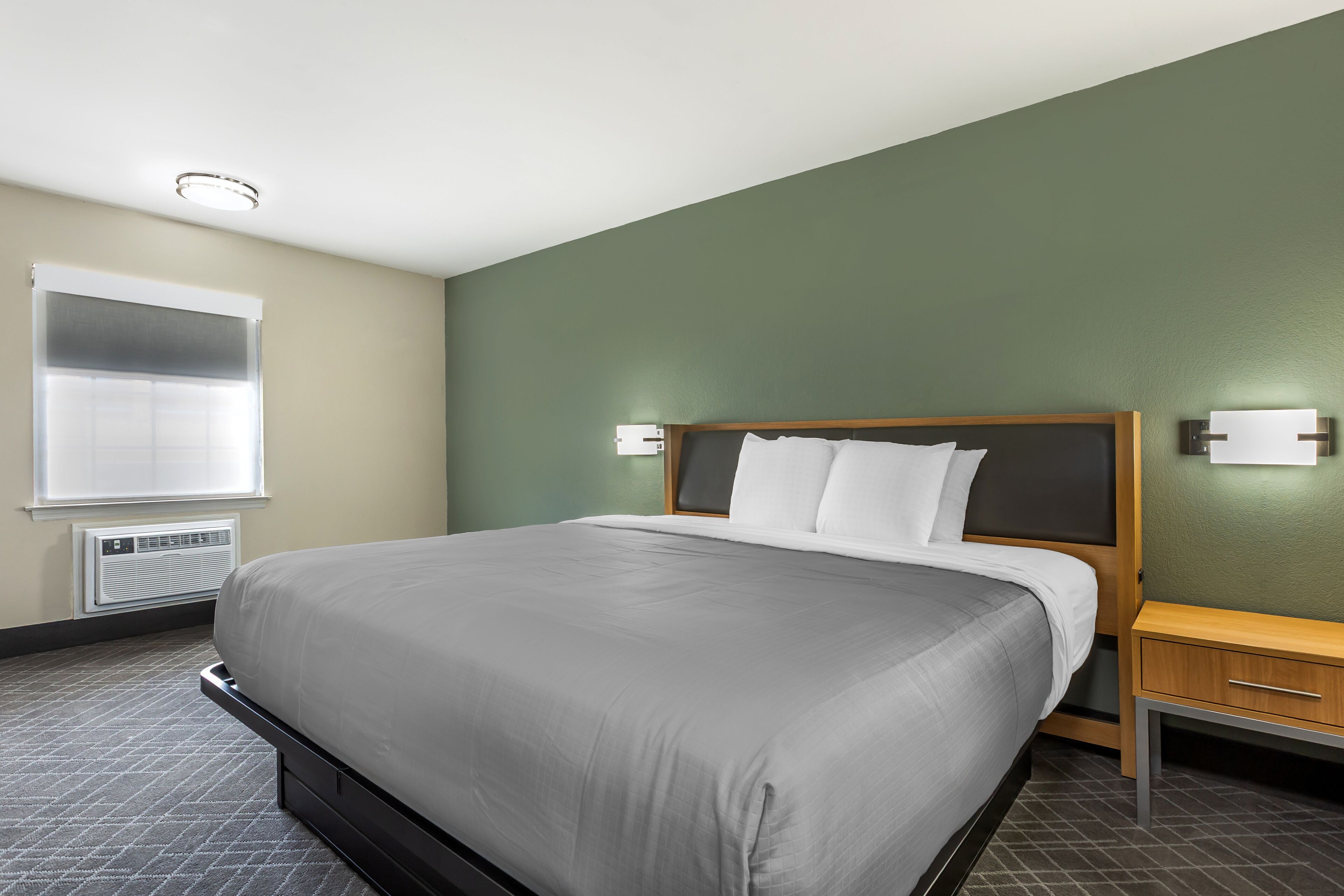 Una habitación de hotel con una cama grande, una mesita de noche y un equipo de aire acondicionado.