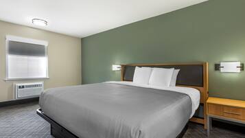 Una habitación de hotel con una cama grande, una mesita de noche y un equipo de aire acondicionado.