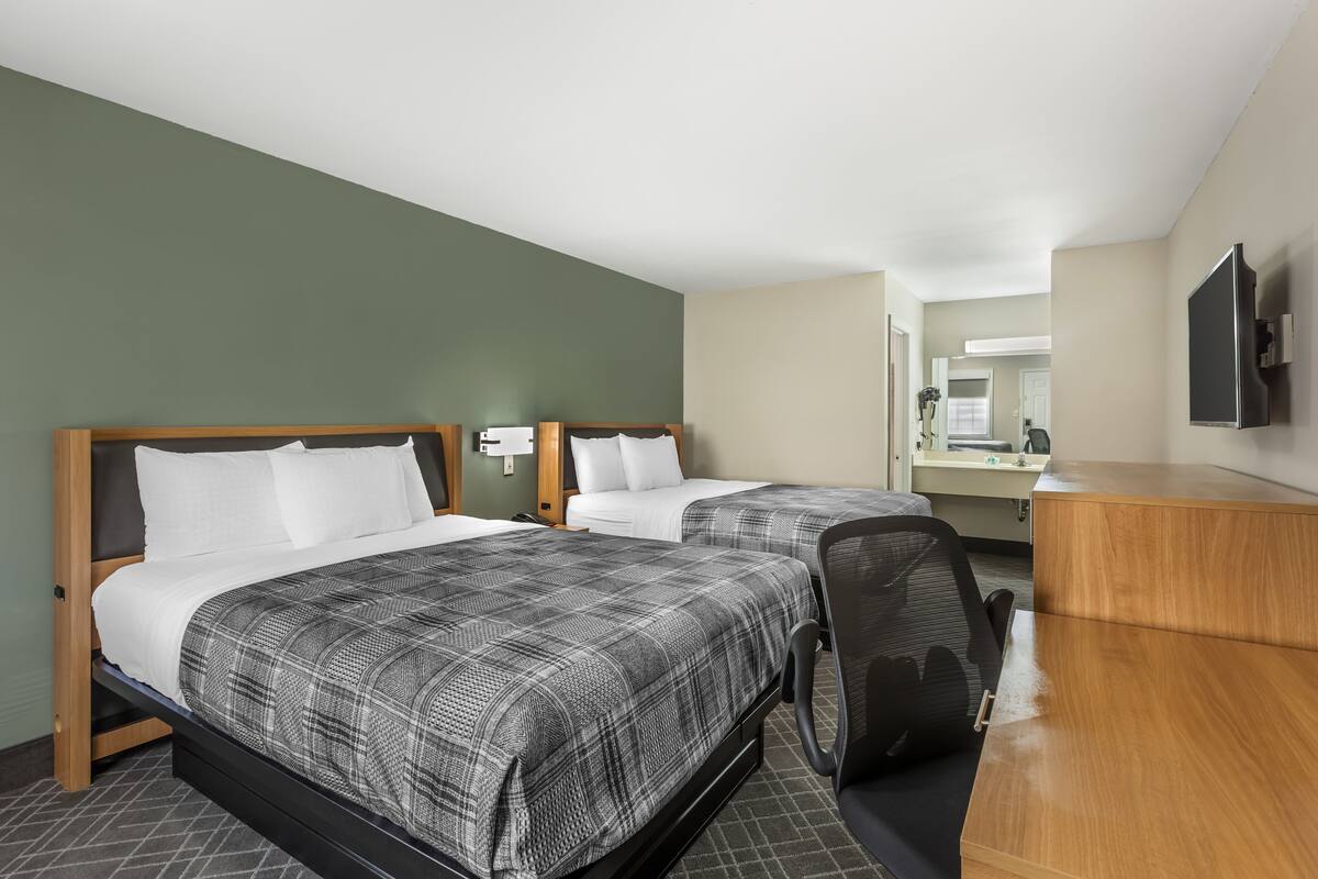 Une chambre d’hôtel avec deux lits, un bureau et un miroir.