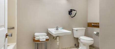 Un baño con inodoro, lavabo y una pequeña mesa con toallas.