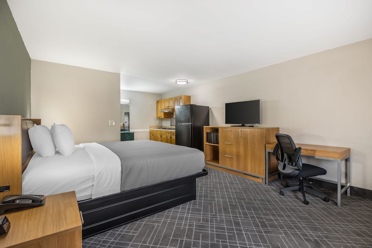 Une chambre d’hôtel équipée d’un lit, d’un bureau, d’une chaise, d’une télévision, d’un réfrigérateur et d’une kitchenette.