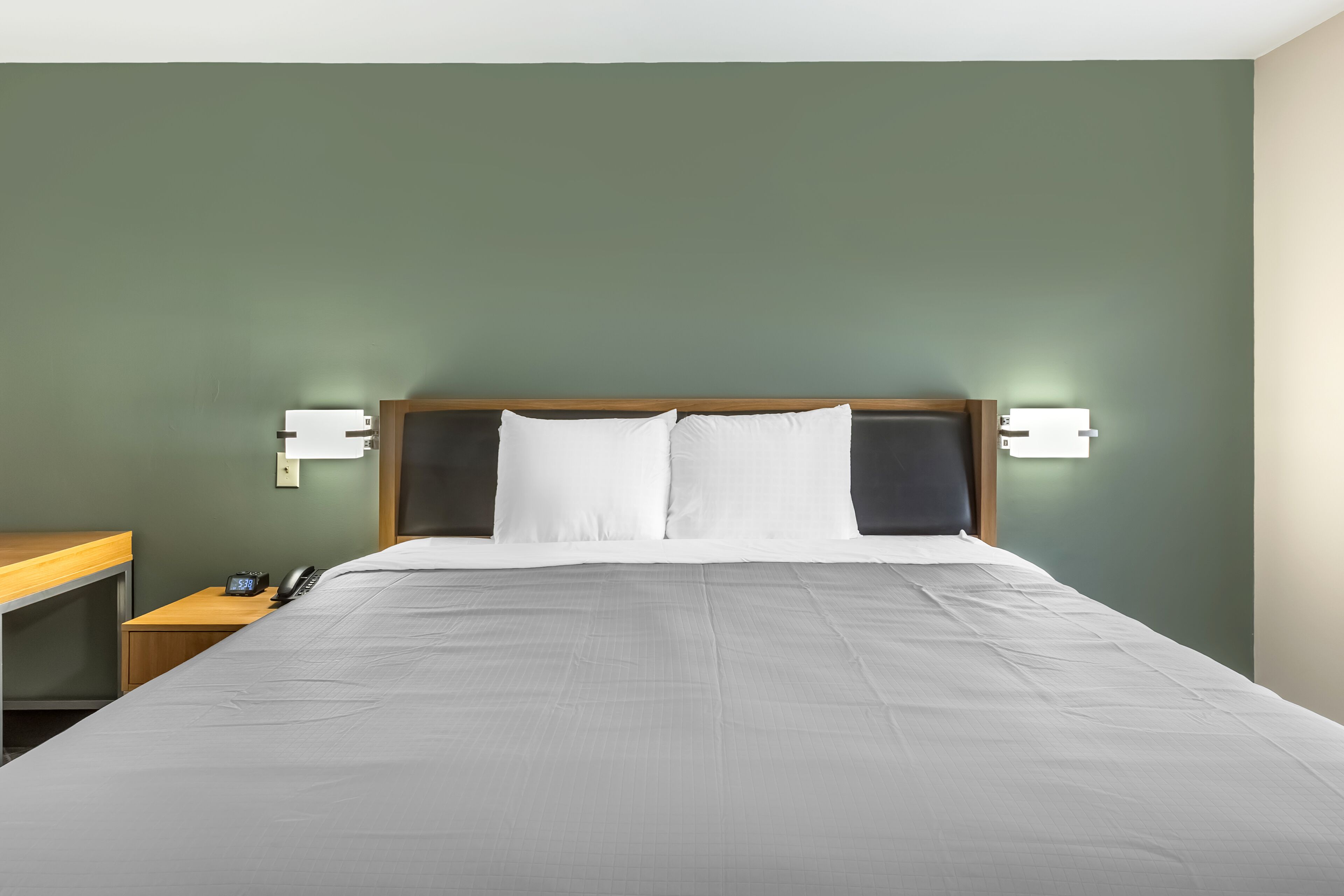 Una habitación de hotel con cama, mesitas de noche y lámparas de pared.